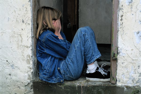 Niña angustiada sentada en una entrada, muestra señales de sufrimiento emocional vinculadas al Síndrome de Alienación Parental.