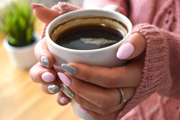 Manos de mujer tomando una taza de café, una de las bebidas a evitar durante la lactancia
