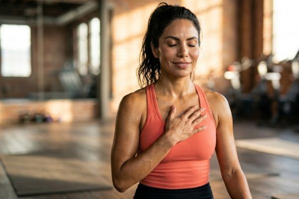 beneficios del body combat Mujer latina con la mano sobre el pecho sintiendo su ritmo cardíaco después de clase de Body Combat, expresión de satisfacción y vitalidad