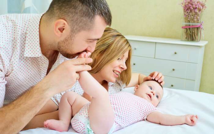 Mamá y papá acarician y juegan con su bebé, aprendiendo juntos el inicio de la experiencia de ser padres