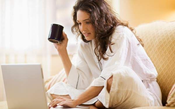 Mujer en casa con su laptop y una taza de café mientras redacta su CV para buscar trabajo remoto