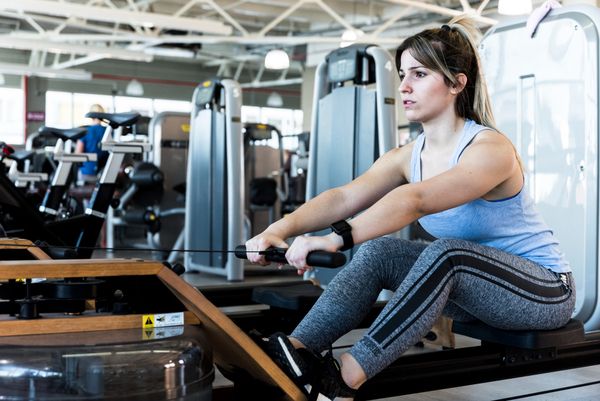 Mujer entrenando en máquina de remo en el gimnasio Planet Fitness® con actitud enfocada y segura.