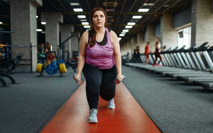 Mujer principiante realizando ejercicio de fuerza con mancuernas en gimnasio, adaptando su rutina de ejercicio a su ritmo y condición física.