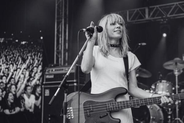 Kim Gordon en concierto, tocando el bajo con fuerza y cantando con su voz áspera, un ícono del rock alternativo.