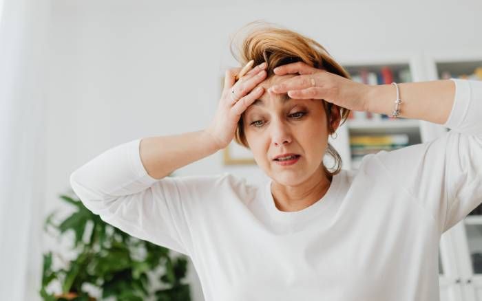 Gemini dijo Una mujer abrumada se toca la cabeza, mostrando el agotamiento y el peso de la carga mental invisible.