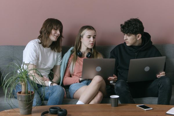  Tres adolescentes sentados en un sofá usando laptops, representando la influencia social y búsqueda de pertenencia.