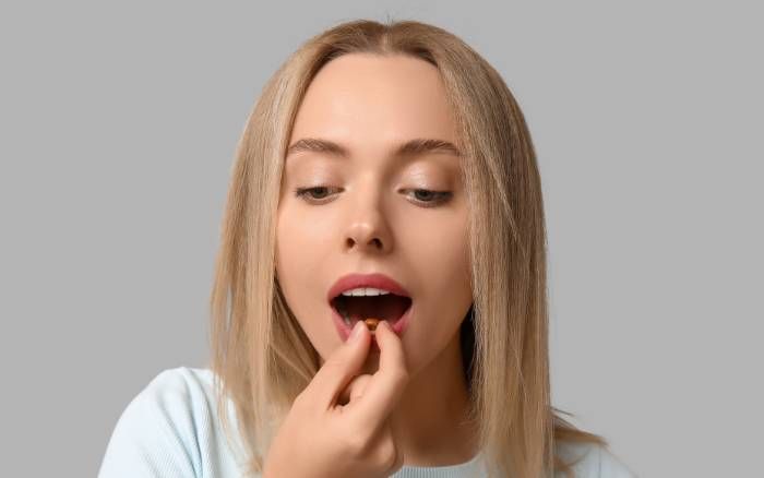Mujer tomando una cápsula de Vitanco® con Rhodiola rosea que ayuda a aliviar fatiga, agotamiento e irritabilidad, regulando el estrés.