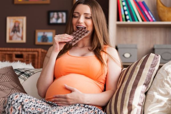 Mujer embarazada comiendo chocolate, un antojo comun en esta etapa.