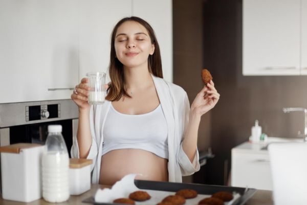 que son los antojos en el embarazo Mujer embarazada tomando leche y galletas cumpliendo un antojo de esta etapa.